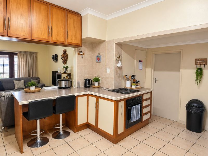Open plan kitchen featuring built-in cabinetry, gas hob, oven, and breakfast bar, seamlessly flowing into the adjacent living area with tiled flooring throughout.