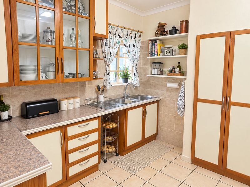 A functional kitchen featuring timber-framed cabinetry, laminate countertops, a double stainless steel sink, and tiled flooring with ample storage space.