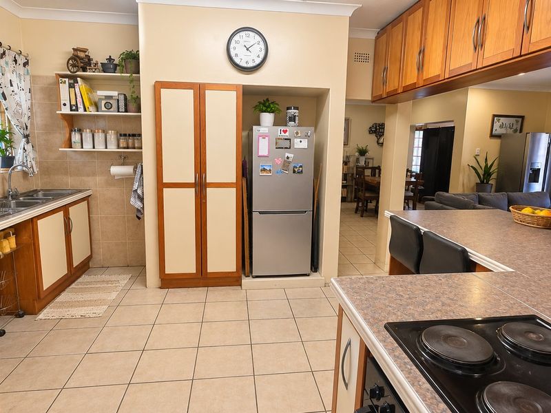A functional kitchen featuring laminate countertops, ample built-in cabinetry, a tiled splashback, and an electric hob, with an open-plan layout connecting to the living area.