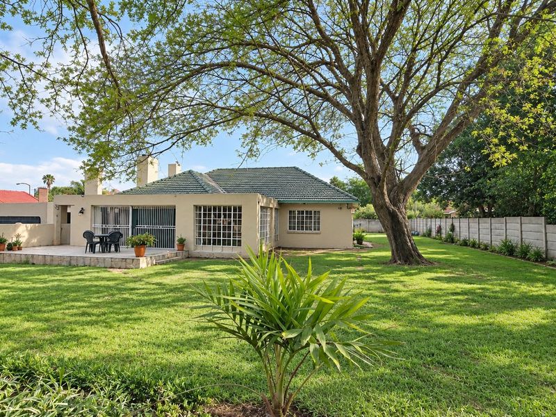 A spacious rear garden featuring a large mature tree, a paved patio area, and secure boundary walls, offering a private outdoor living space.