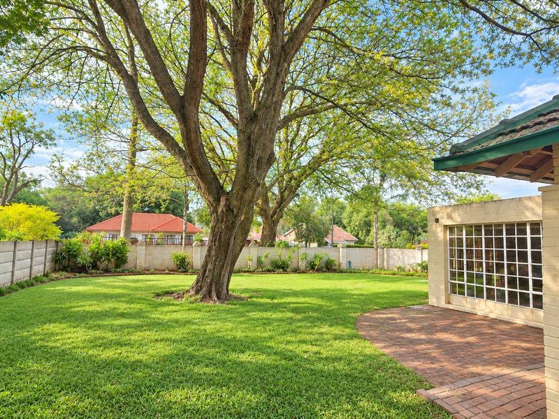 A well-maintained rear garden featuring a lush lawn, mature tree, brick boundary wall, and a paved patio area adjacent to the house.