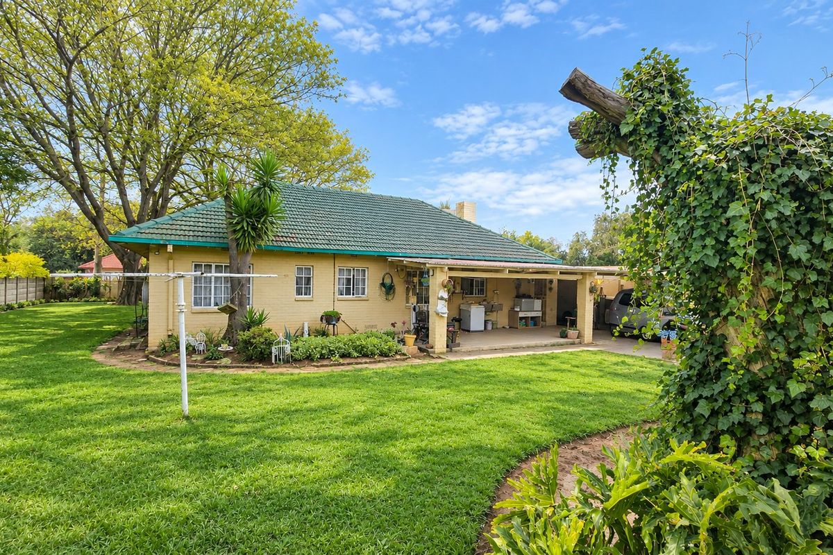Rear view of a single-story brick house featuring a tiled roof, a covered patio area, and a spacious, well-maintained garden.