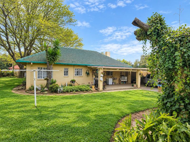 Rear view of a single-story brick house featuring a tiled roof, a covered patio area, and a spacious, well-maintained garden.