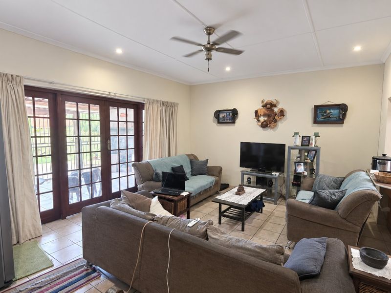 Open plan living area featuring tiled floors, a ceiling fan, and direct access to the patio through double glass doors.