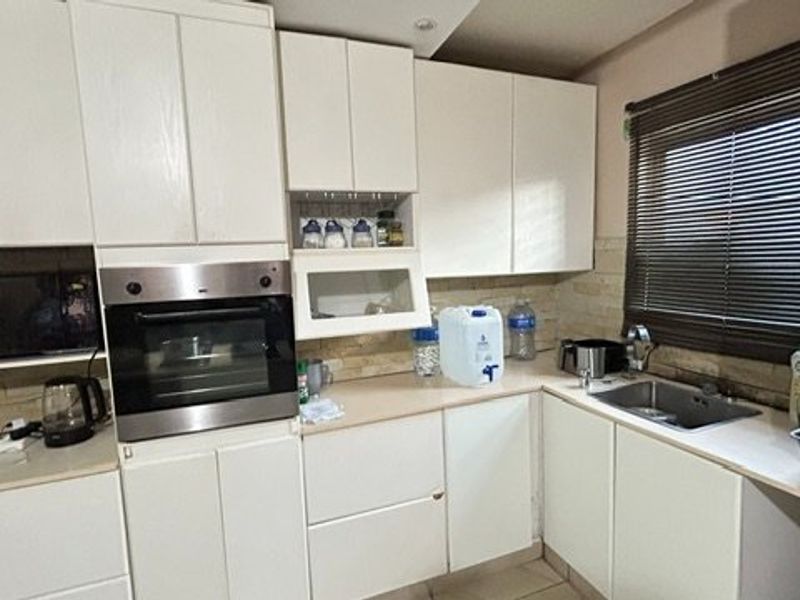 A functional kitchen featuring white cabinetry, built-in oven and microwave, laminate countertops, and a stainless steel sink with a window view.