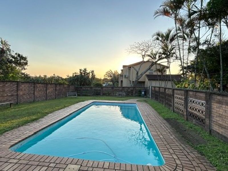 A private outdoor pool area featuring a rectangular swimming pool surrounded by brick paving and enclosed by a secure brick boundary wall.