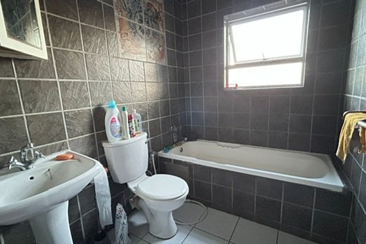 A dated bathroom featuring dark wall tiles, a pedestal basin, a standard toilet, and a built-in bathtub with a top-hung window.
