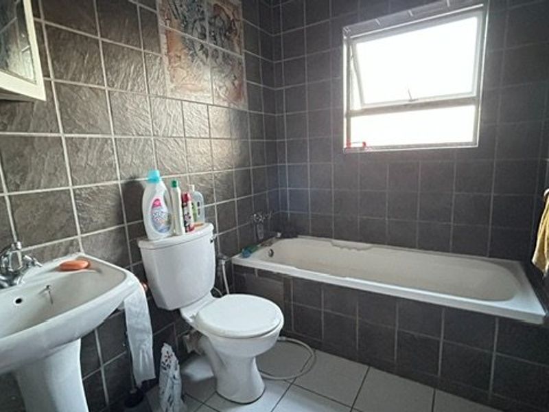 A dated bathroom featuring dark wall tiles, a pedestal basin, a standard toilet, and a built-in bathtub with a top-hung window.