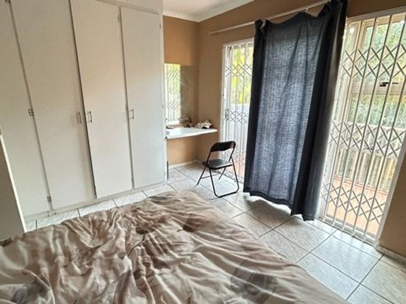 A bedroom featuring built-in cupboards, a vanity area, and direct access to an outdoor space through a sliding door with a security gate.
