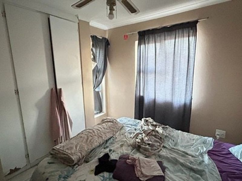 A bedroom featuring a built-in wardrobe with visible wear and a ceiling fan, offering a functional space with potential for cosmetic updates.