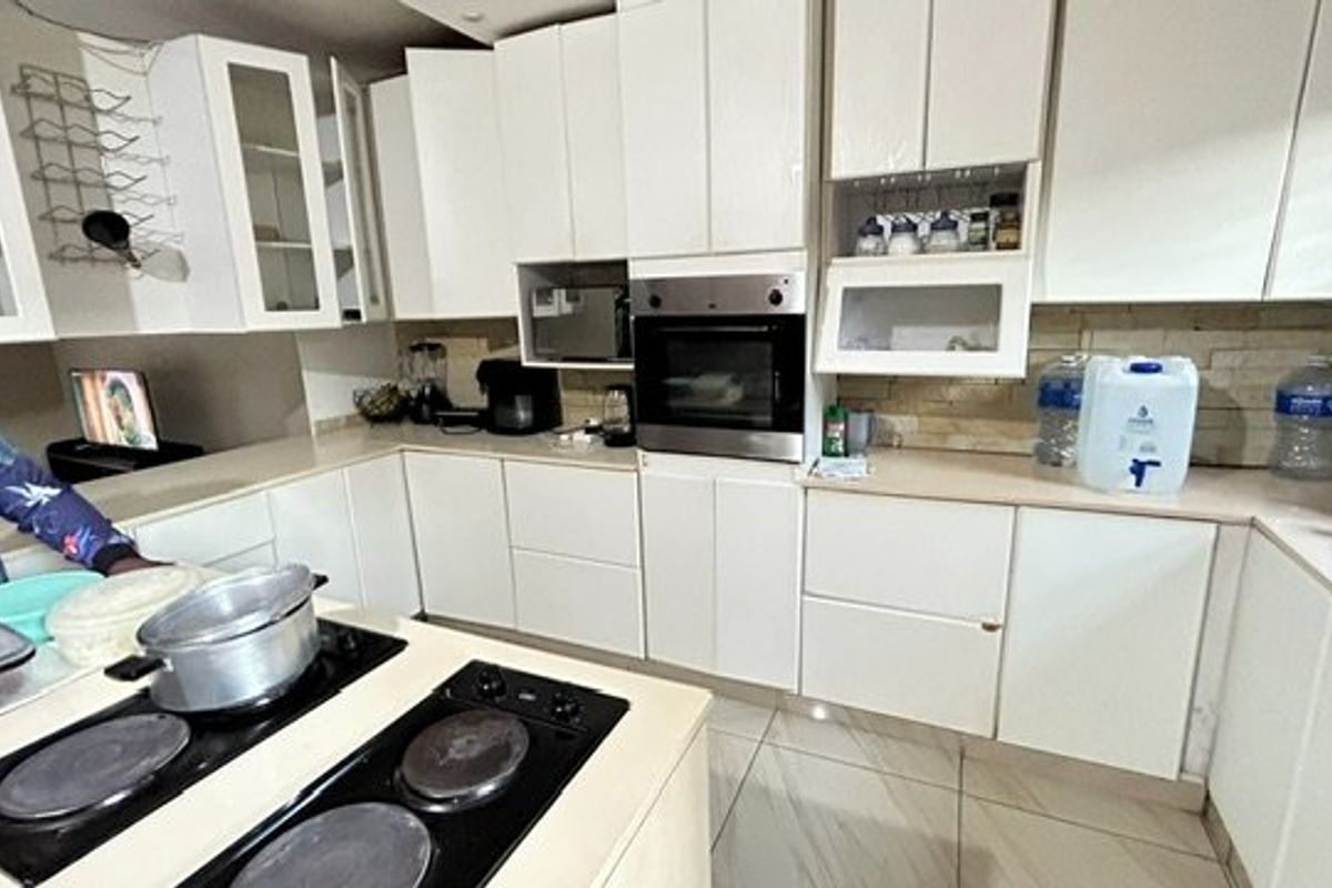 A functional kitchen featuring white cabinetry, stone countertops, a built-in oven, and an integrated electric hob with tiled flooring throughout.