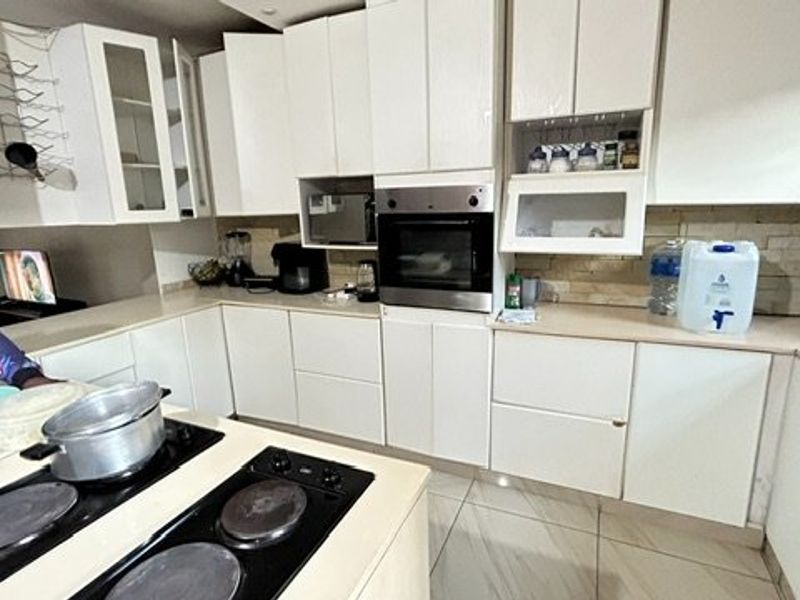 A functional kitchen featuring white cabinetry, stone countertops, a built-in oven, and an integrated electric hob with tiled flooring throughout.