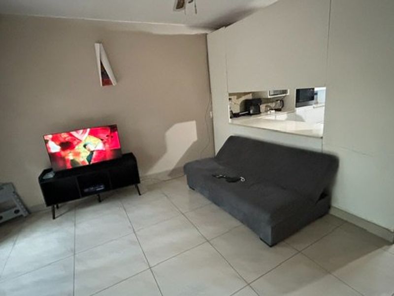 A living area featuring tiled flooring and a pass-through window connecting to the kitchen, with security gate access to the exterior.