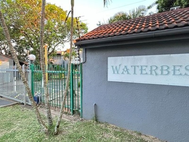 View of the complex entrance featuring a perimeter wall, security gate, and electric fencing.