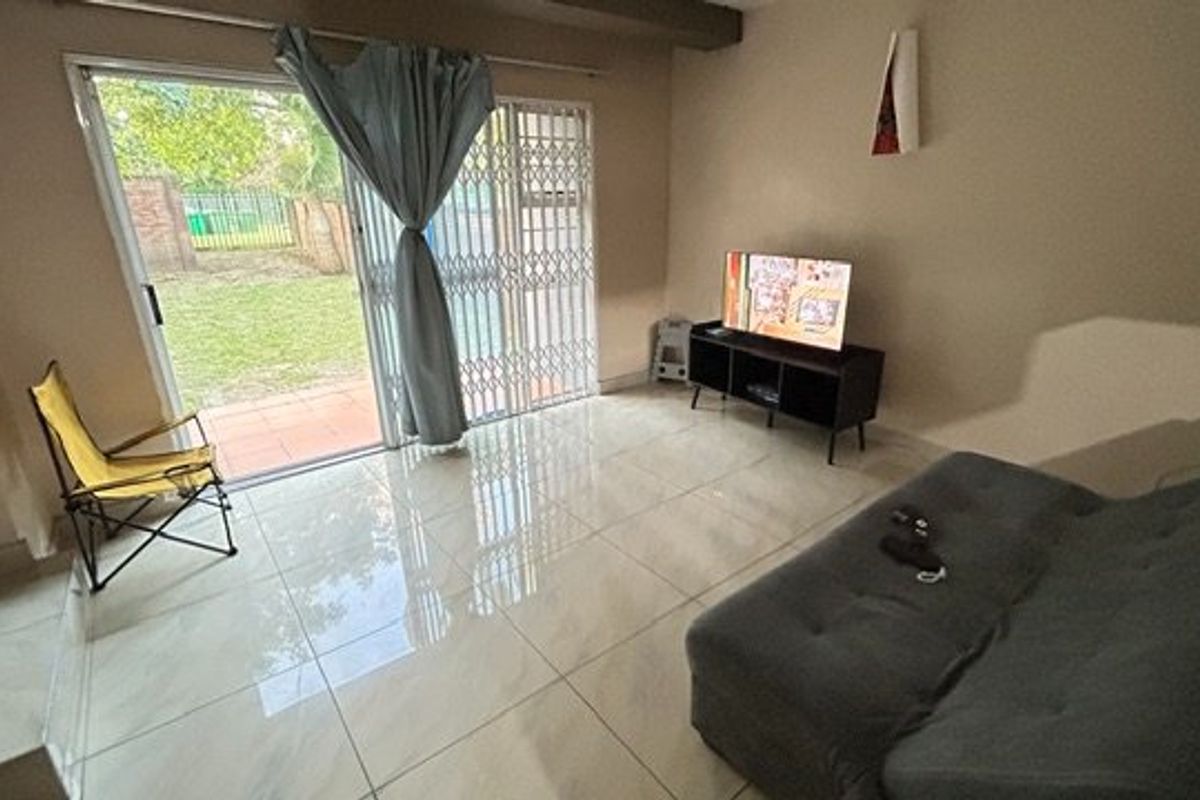 A living room featuring large format tiled flooring and a sliding glass door with a security gate providing access to the rear garden.