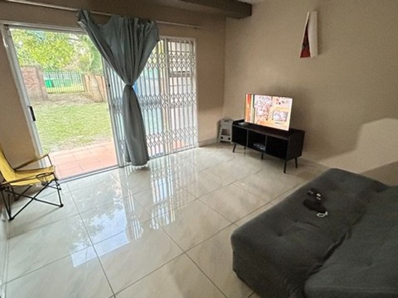A living room featuring large format tiled flooring and a sliding glass door with a security gate providing access to the rear garden.