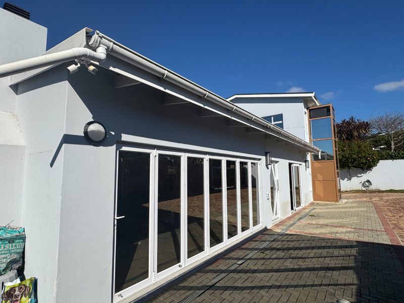 Rear exterior view of the property featuring extensive bi-fold doors, paved patio area, and a modern glass elevator shaft.