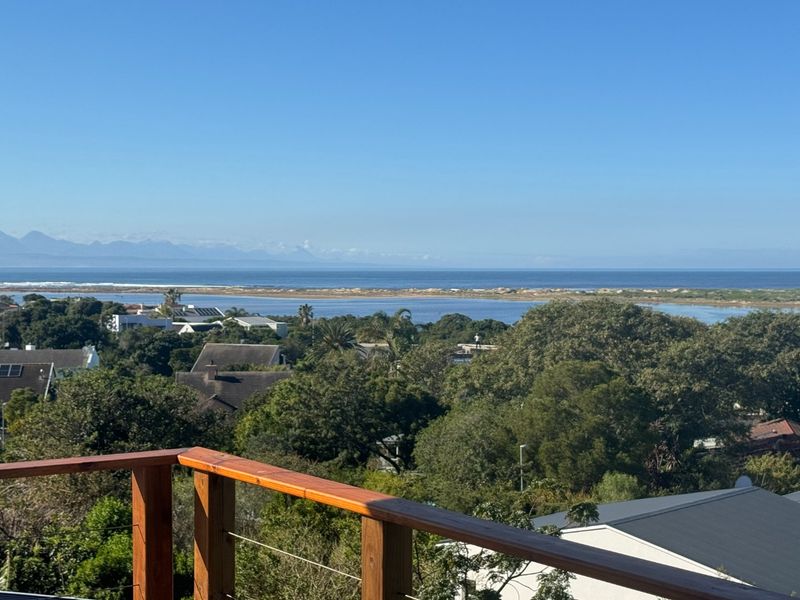 Elevated outdoor view featuring a timber balustrade overlooking a scenic coastal landscape with ocean and mountain vistas.