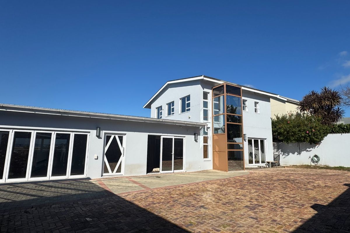 Rear exterior view of the property featuring a paved courtyard, modern glass elevator shaft, and multiple access points via bi-fold and sliding doors.