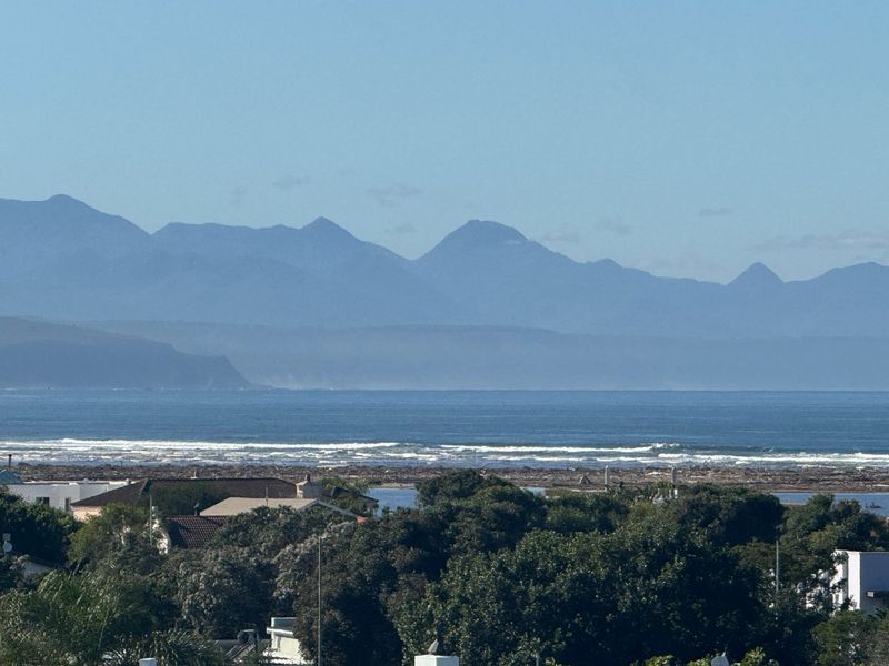 A scenic elevated view overlooking the coastline, ocean, and distant mountain range.