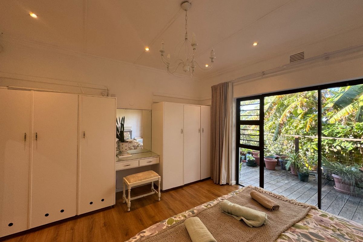 Spacious bedroom featuring built-in cupboards, an integrated vanity, and large sliding glass doors opening onto a private balcony with lush garden views.