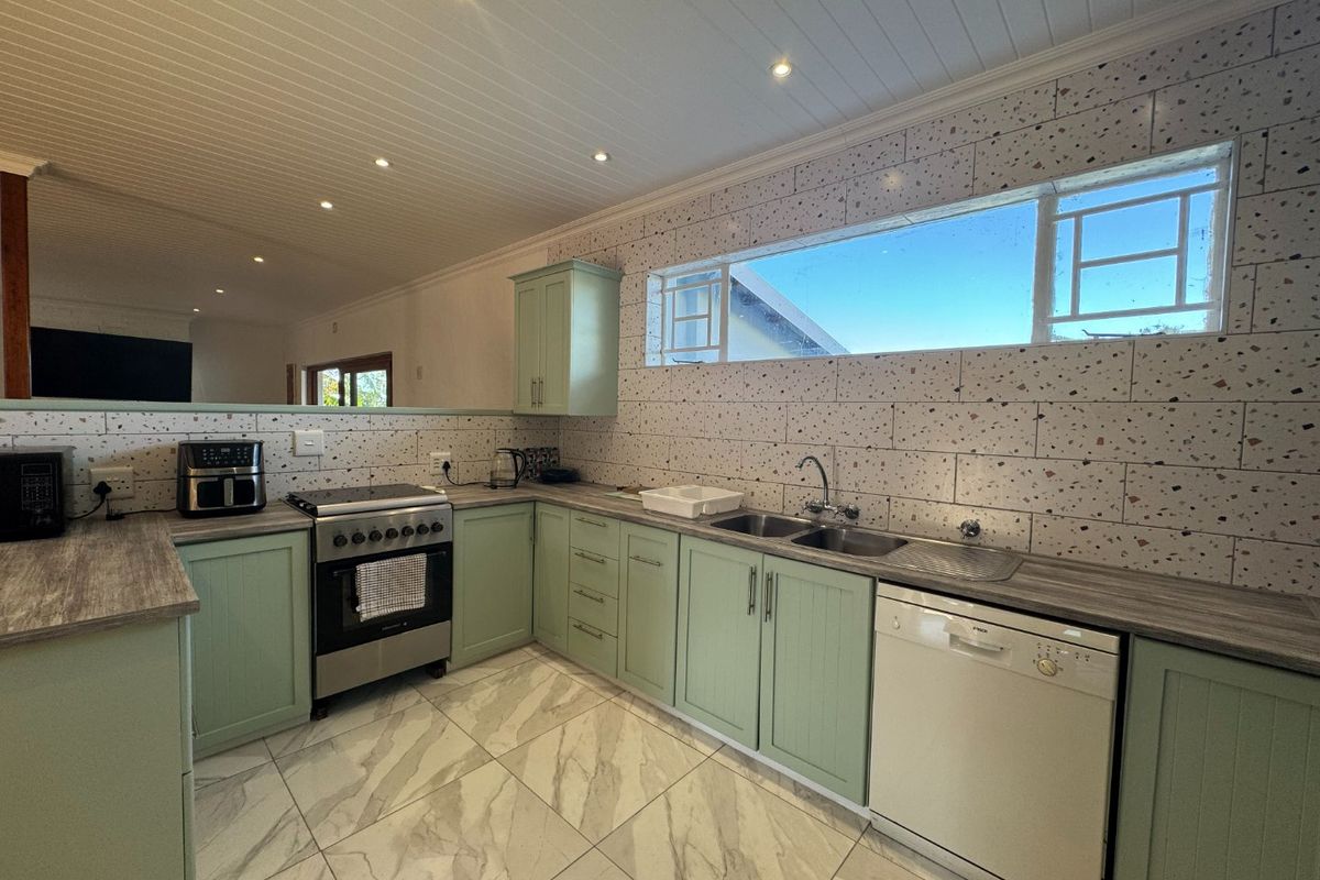Modern kitchen featuring sage green cabinetry, terrazzo-style wall tiling, marble-look flooring, and a functional layout with integrated sink and stove.