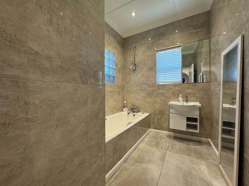 A modern, fully tiled bathroom featuring a built-in bathtub, wall-mounted vanity, and a combination of glass block and standard windows for natural light.