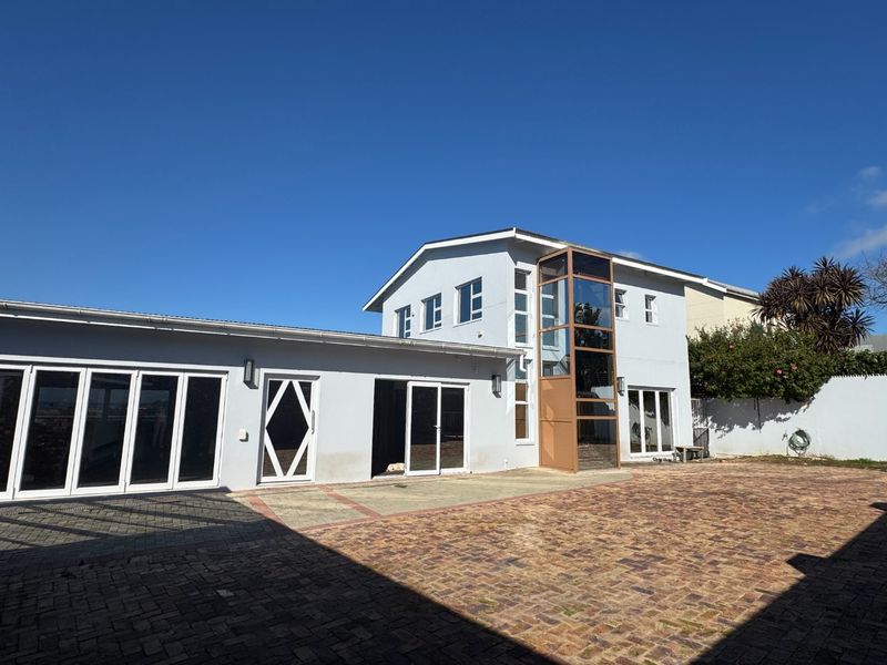 Rear exterior view of the property featuring a paved courtyard, modern glass elevator shaft, and multiple access points via bi-fold and sliding doors.