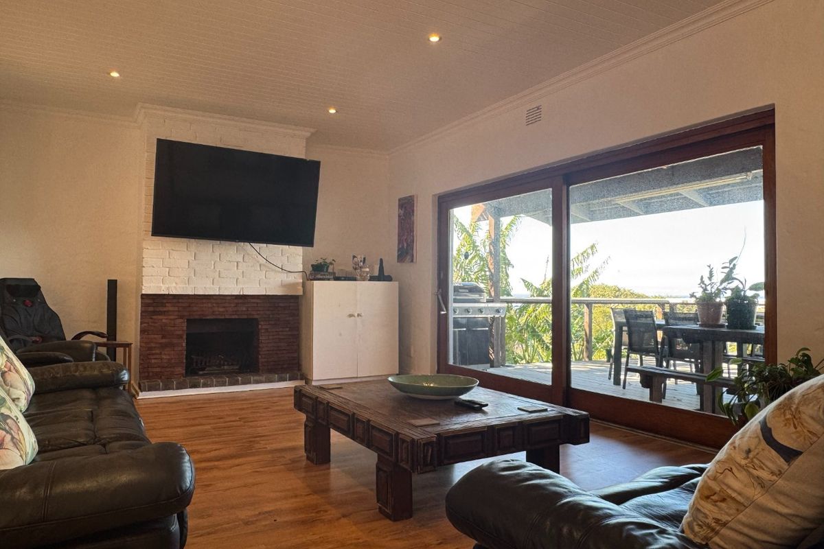 Spacious living room featuring a brick fireplace, wood-look flooring, and large sliding glass doors that open onto an outdoor patio area.