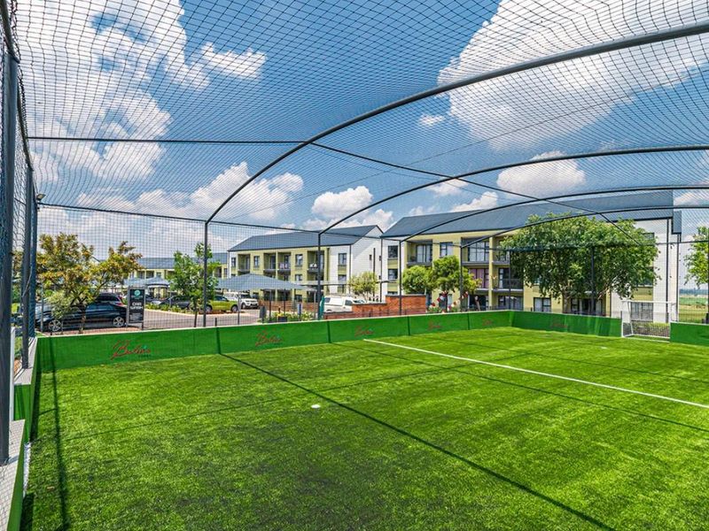 A well-maintained outdoor artificial turf sports court enclosed with perimeter netting and fencing, located within the apartment complex grounds.
