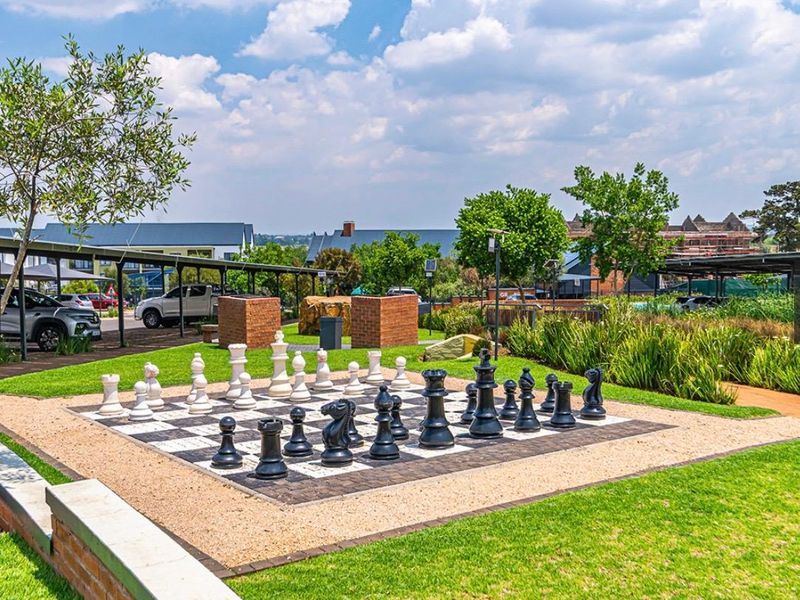 Well-maintained communal garden area featuring a large outdoor chess board, manicured lawn, and brick landscaping elements within an apartment complex.