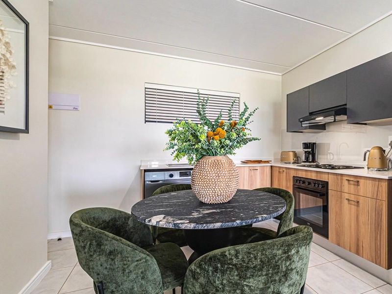 Modern open-plan kitchen featuring wood-grain cabinetry, dark overhead cupboards, integrated appliances, and tiled flooring, seamlessly flowing into the dining area.