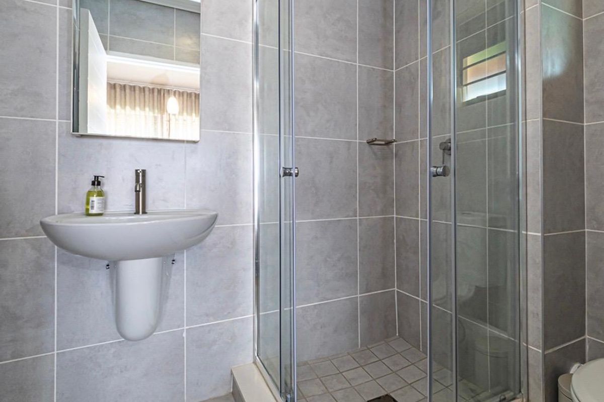 A clean, modern bathroom featuring a wall-mounted basin, a glass-enclosed shower, and neutral grey wall and floor tiling.