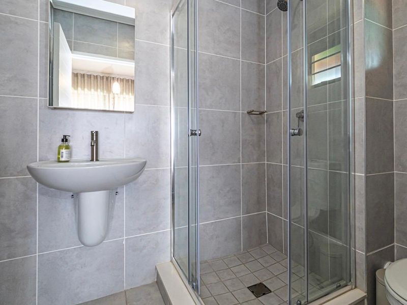 A clean, modern bathroom featuring a wall-mounted basin, a glass-enclosed shower, and neutral grey wall and floor tiling.