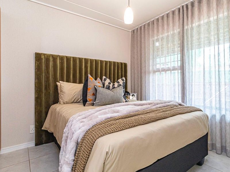 A well-maintained bedroom featuring tiled flooring, neutral wall finishes, and large windows with installed curtain tracks, providing a bright and comfortable living space.