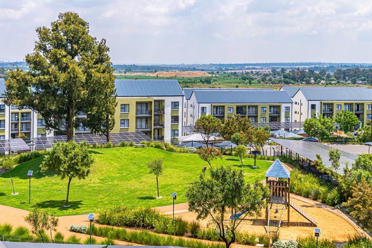 Elevated view of a well-maintained residential apartment complex featuring landscaped gardens, a children's playground, and extensive solar panel installations.