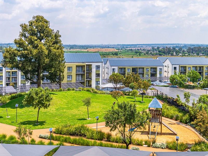 Elevated view of a well-maintained residential apartment complex featuring landscaped gardens, a children's playground, and extensive solar panel installations.