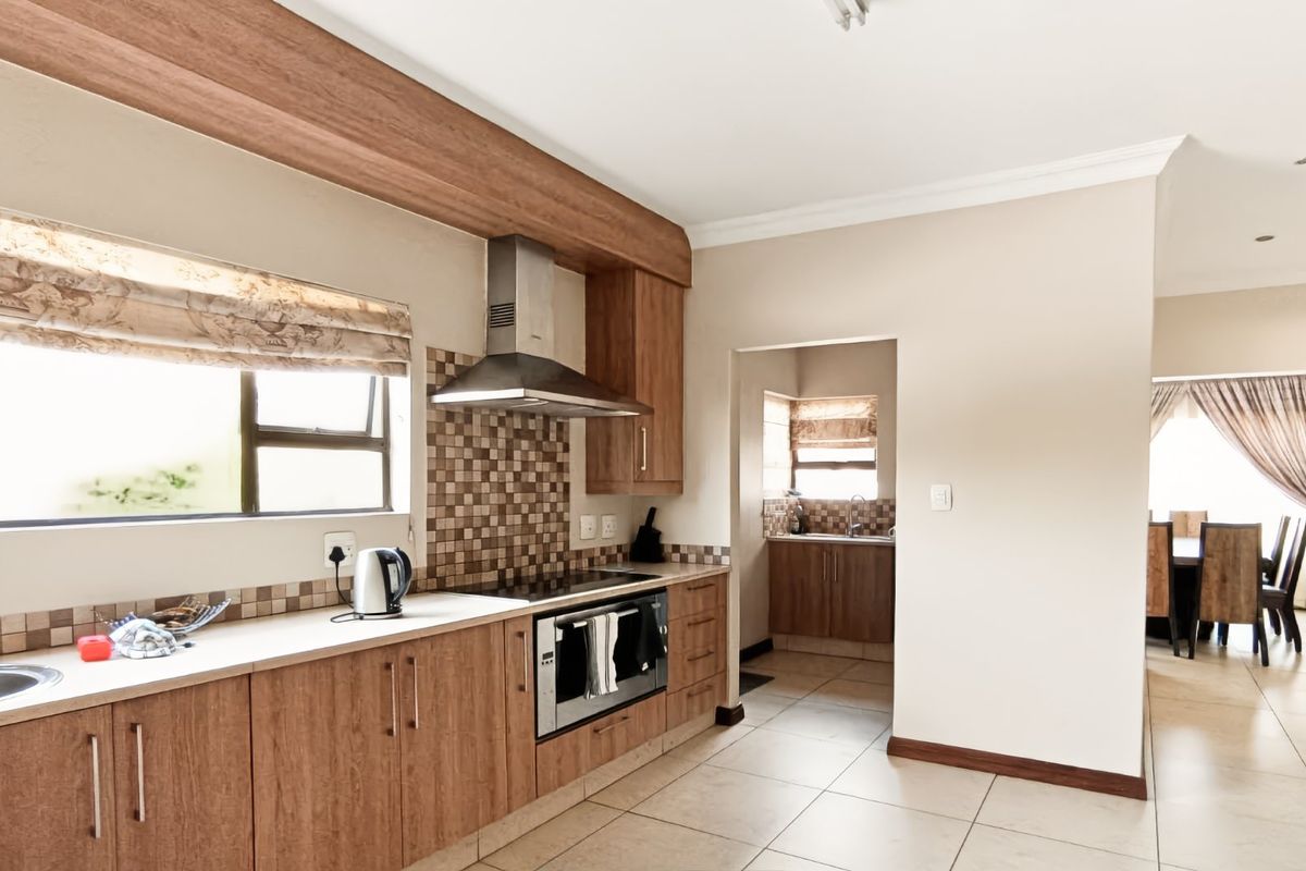 A functional kitchen featuring wood-finish cabinetry, a built-in oven with hob, stainless steel extractor fan, and tiled splashbacks, with an adjacent scullery area.