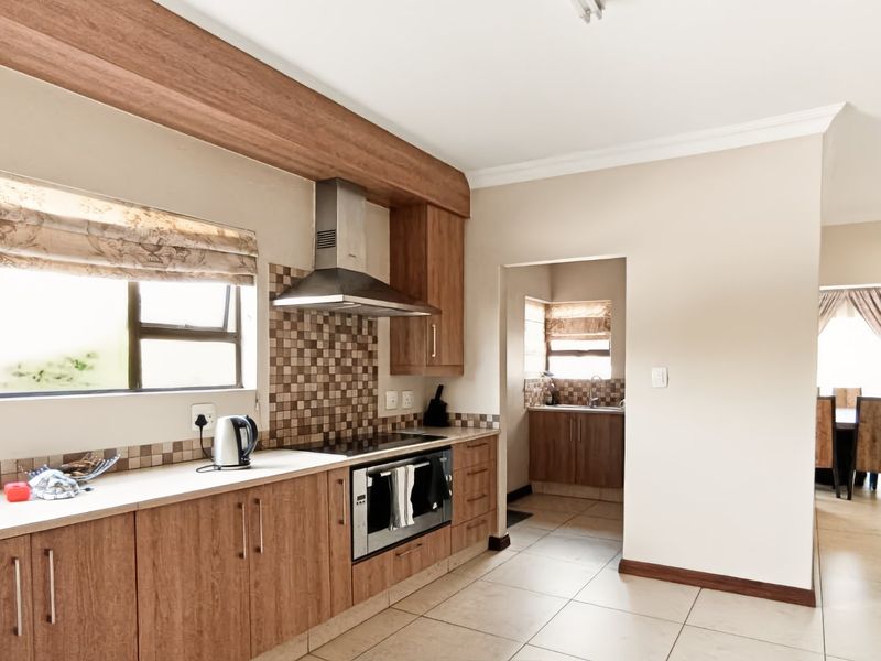 A functional kitchen featuring wood-finish cabinetry, a built-in oven with hob, stainless steel extractor fan, and tiled splashbacks, with an adjacent scullery area.