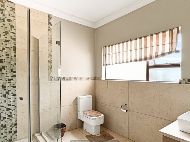 A modern bathroom featuring a glass-enclosed shower with mosaic tile accents, a vessel sink, and neutral ceramic tiling throughout.
