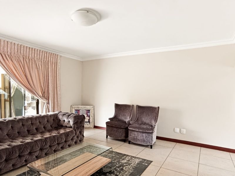 A bright living room featuring neutral tiled flooring, decorative ceiling cornicing, and a large sliding glass door providing access to the exterior.