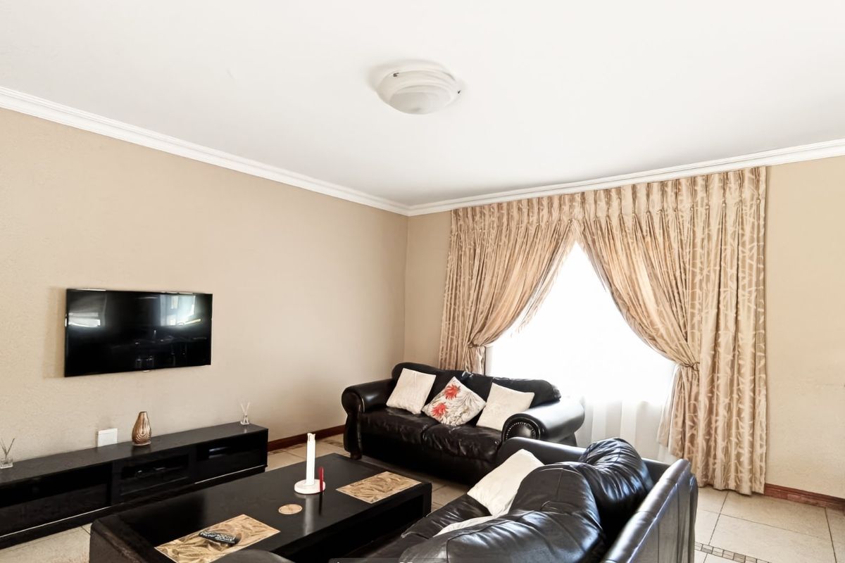 A comfortable living room featuring neutral wall tones, tiled flooring, and classic ceiling cornicing, providing a functional and inviting space for relaxation.