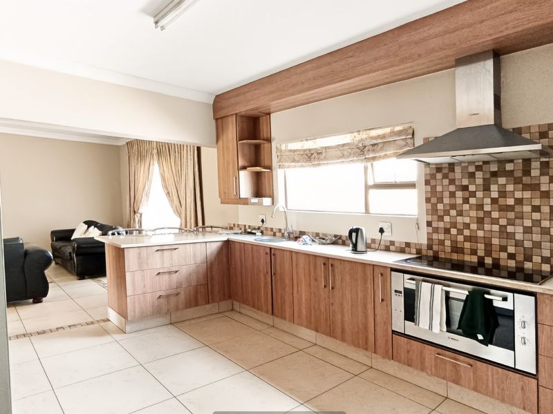 Open-plan kitchen featuring wood-look cabinetry, stone countertops, mosaic backsplash, and integrated stainless steel appliances, flowing into an adjacent living area.