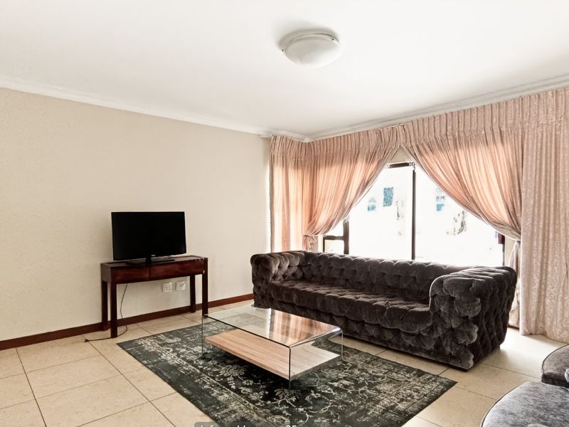 A bright living room featuring neutral tiled flooring, coved ceilings, and a large sliding glass door providing natural light.