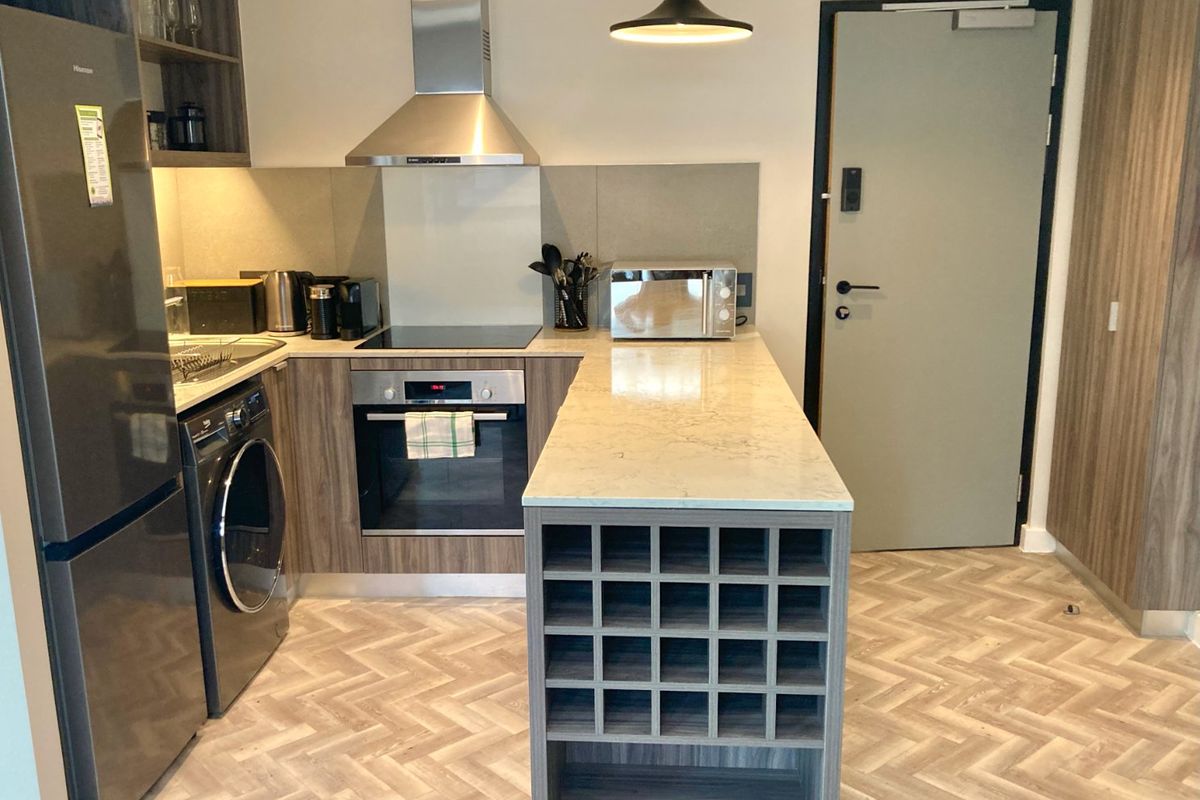Modern kitchen featuring stone countertops, built-in oven, electric hob, extractor fan, and a custom wine rack, complemented by stylish herringbone flooring.