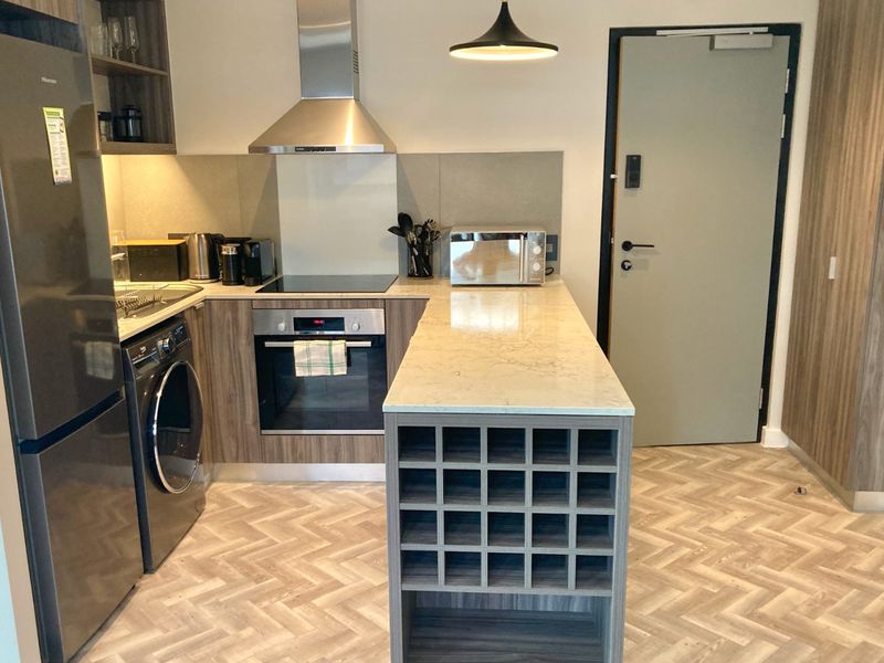 Modern kitchen featuring stone countertops, built-in oven, electric hob, extractor fan, and a custom wine rack, complemented by stylish herringbone flooring.