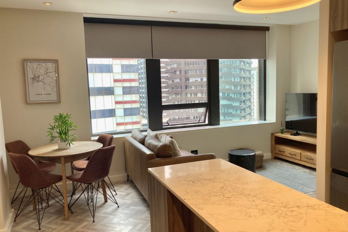 Modern open-plan living and dining area featuring elegant herringbone flooring, a stone-topped kitchen island, and large windows with city views.