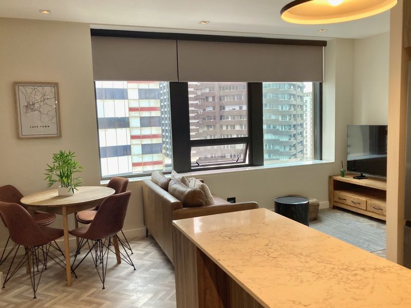 Modern open-plan living and dining area featuring elegant herringbone flooring, a stone-topped kitchen island, and large windows with city views.