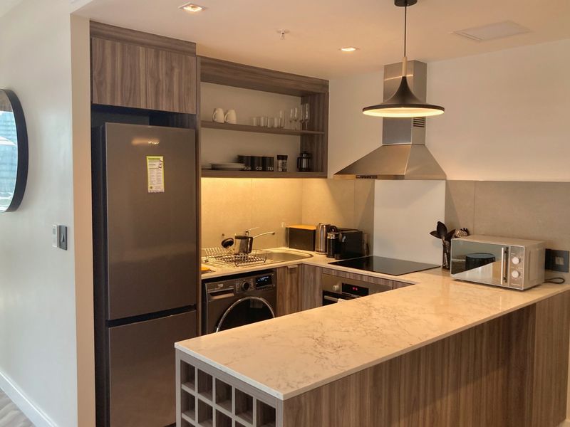 Modern kitchen featuring wood-grain cabinetry, stone countertops, integrated appliances, and a breakfast bar with built-in wine storage.