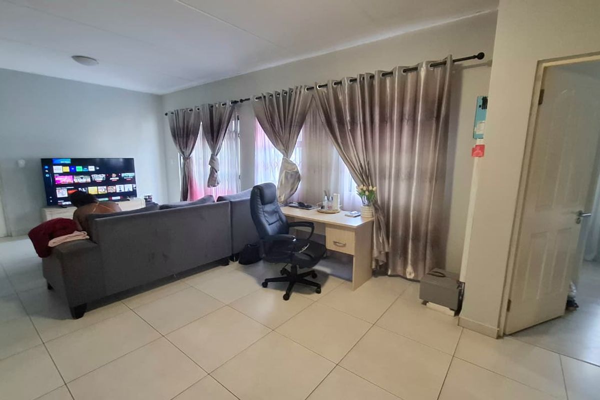 A spacious living area featuring neutral tiled flooring and large windows dressed with curtain rods, offering a functional and open layout.